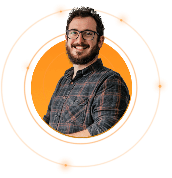 A person with glasses and a beard smiles at the camera. They are wearing a plaid shirt, and the background features an orange circle with a circular, atom-like design.
